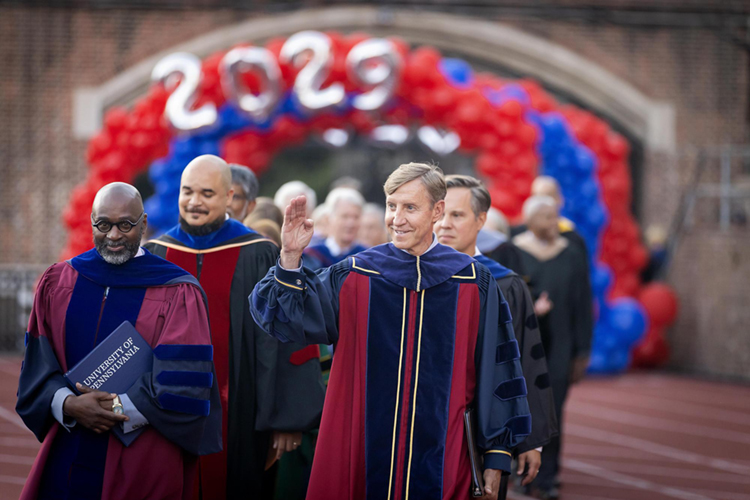 caption: President J. Larry Jameson waves while entering Convocation.