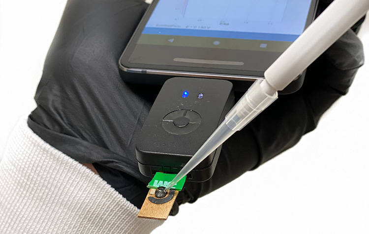 caption: Created in the lab of Dr. de la Fuente and licensed through PCI, this miniaturized, portable version of a rapid COVID-19 test is compatible with smart devices and can detect SARS-CoV-2 within four minutes with nearly 100% accuracy. Photo courtesy of César de la Fuente.