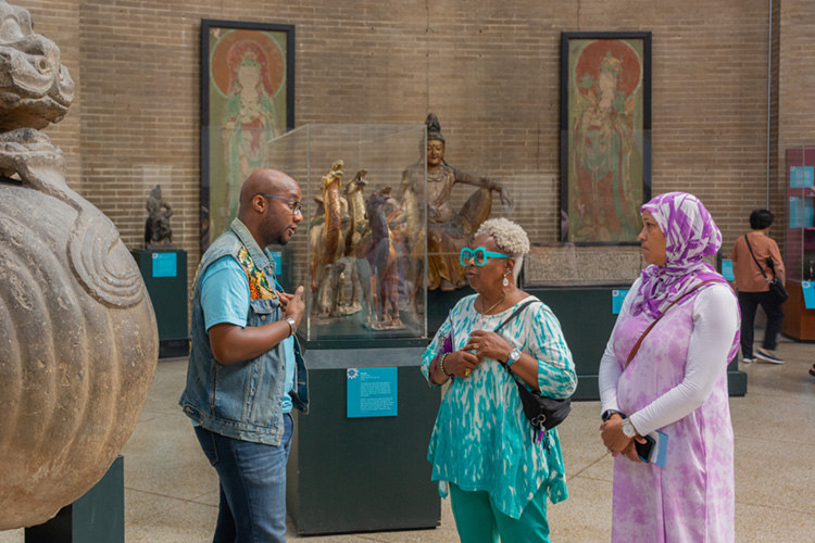caption: Museum Educator Paul Best shares stories with visitors inside the Asia Galleries at the Penn Museum.
