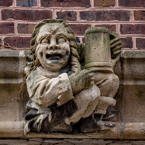 caption: In a representation of student life that is still relevant today, this figure on the exterior of the Quad drinks beer from a mug!
