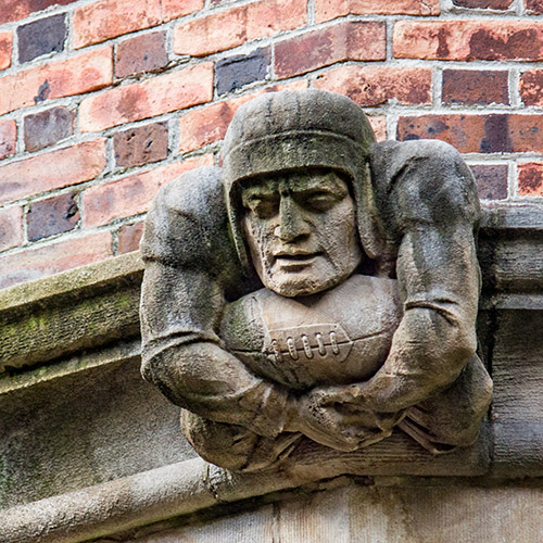 caption: This football player, situated on the exterior of the Quad, visually represents the vigor of early-20th century collegiate life. 