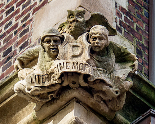 caption: This trio, who adorn a corner on the Quad exterior, hold aloft a P (for Penn) and the University’s motto from 1898 to 1932, Literae Sine Moribus Vanae (letters without morals [are] useless). Today’s motto is slightly different. The owl, a symbol of wisdom, is a common motif throughout Penn’s gargoyles and bosses. 
