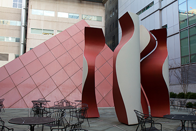 caption: Quadrature #1 by professor emeritus Robert Engman is 16 x 4 x 4 square feet and made of four irregular, painted pieces of mild steel, which are in front of a gridded pyramid-shaped MRI. It was built in 1977 and installed at T. G. Miller Plaza at HUP.