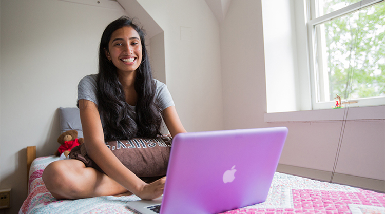 Woman on bed, typing on a laptop, smiling