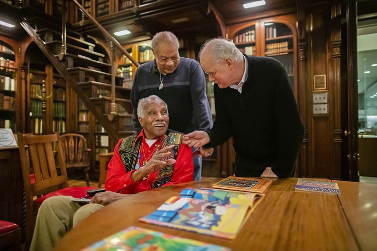 caption:Ashley Bryan (seated) with his nephew Sandy Campbell (left) and David McKnight (right), director of Penn’s Rare Book & Manuscript  Library, during a visit to the Penn Libraries  in January 2019. 