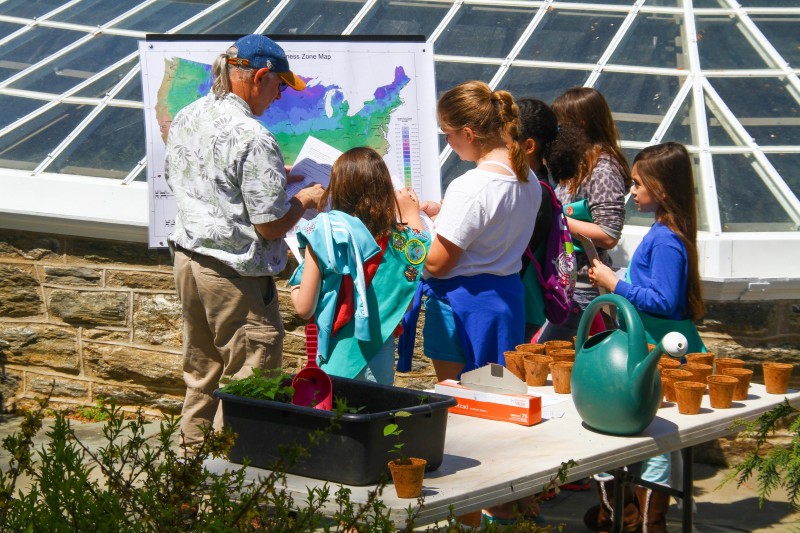 caption: Branch out as a naturalist and dig into learning about trees at Morris Arboretum’s Arbor Day Family Day. Pictured here during this event in 2013, Arboretum volunteer Howard Goldstein explained to Scouts the Hardiness Zone Map of the United Sates, which is a guide to determine the best area for successful plant growth.