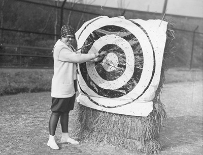 caption: Women’s archery practice session in 1938; Virginia Wingert removing arrows from target.